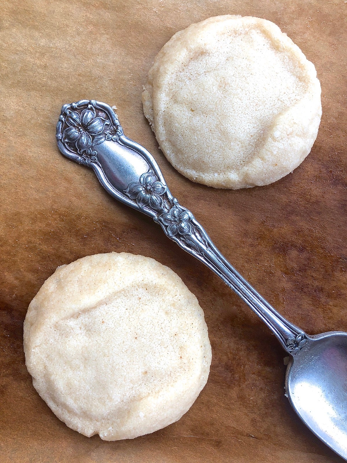 Two baked shortbread cookies with only a vague imprint, shown with the scrolled spoon handle that made the imprint.